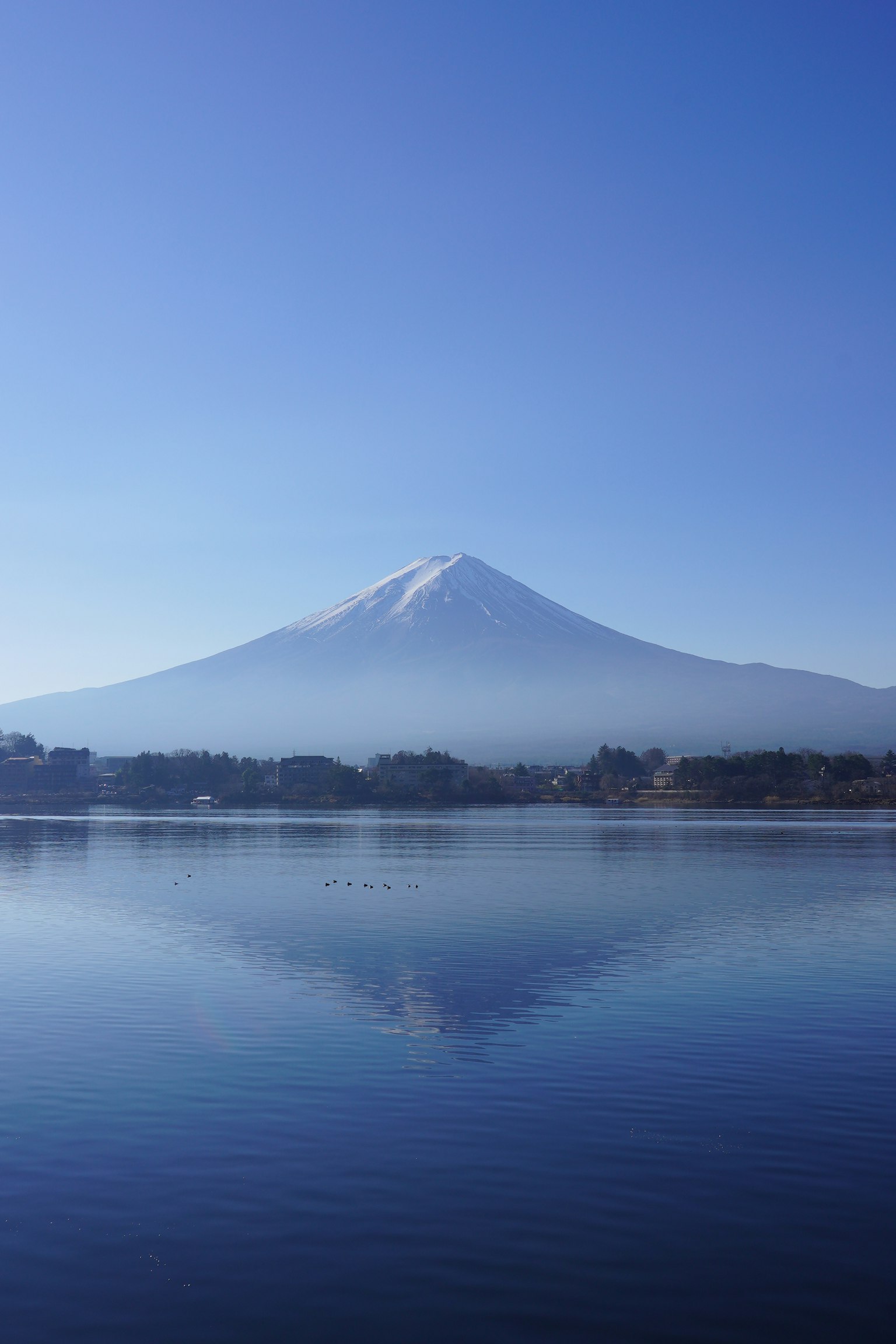 Vista escénica del Monte Fuji con su cumbre nevado reflejada en un lago tranquilo bajo un cielo azul claro