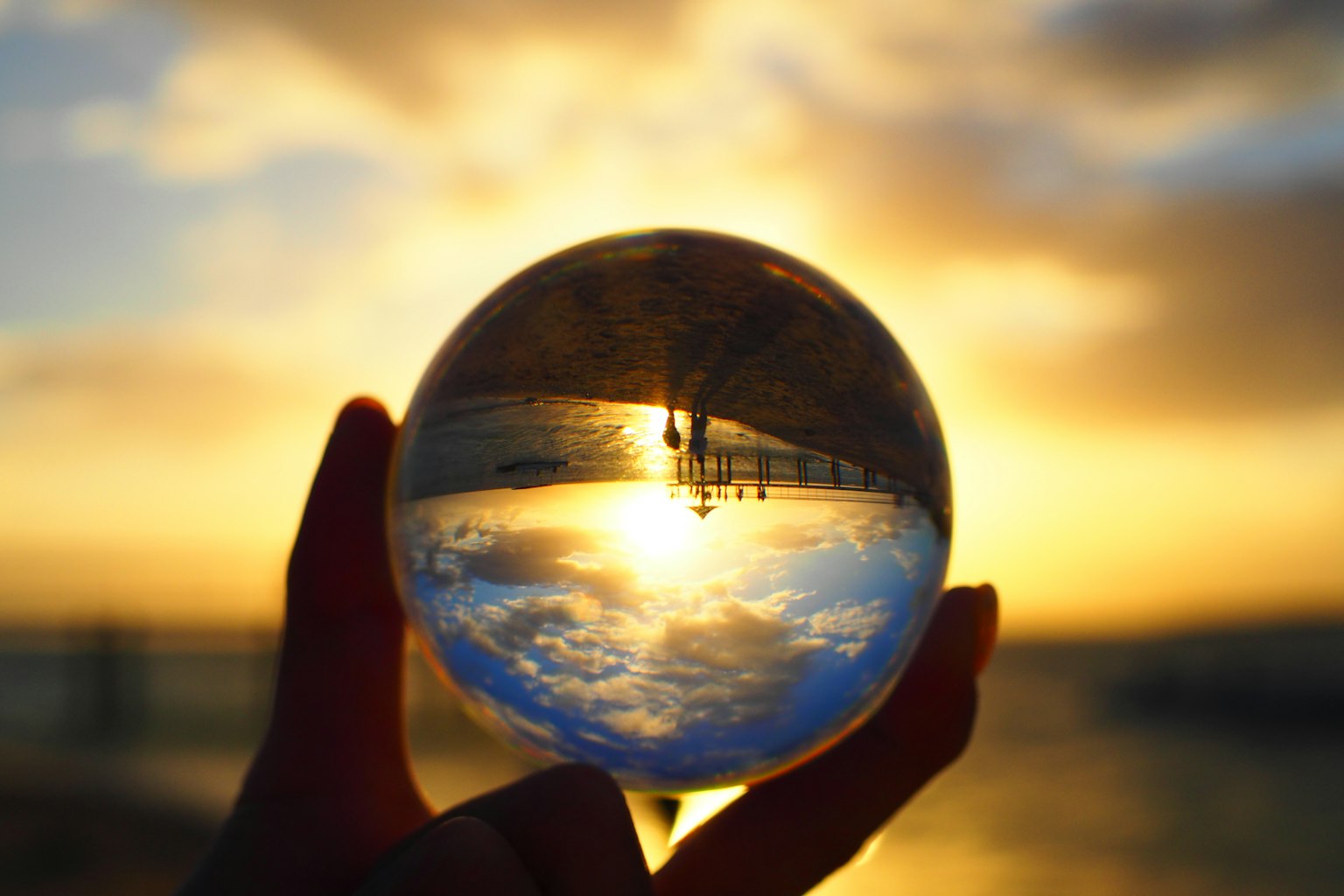Mano che tiene una sfera di cristallo che riflette persone e tramonto