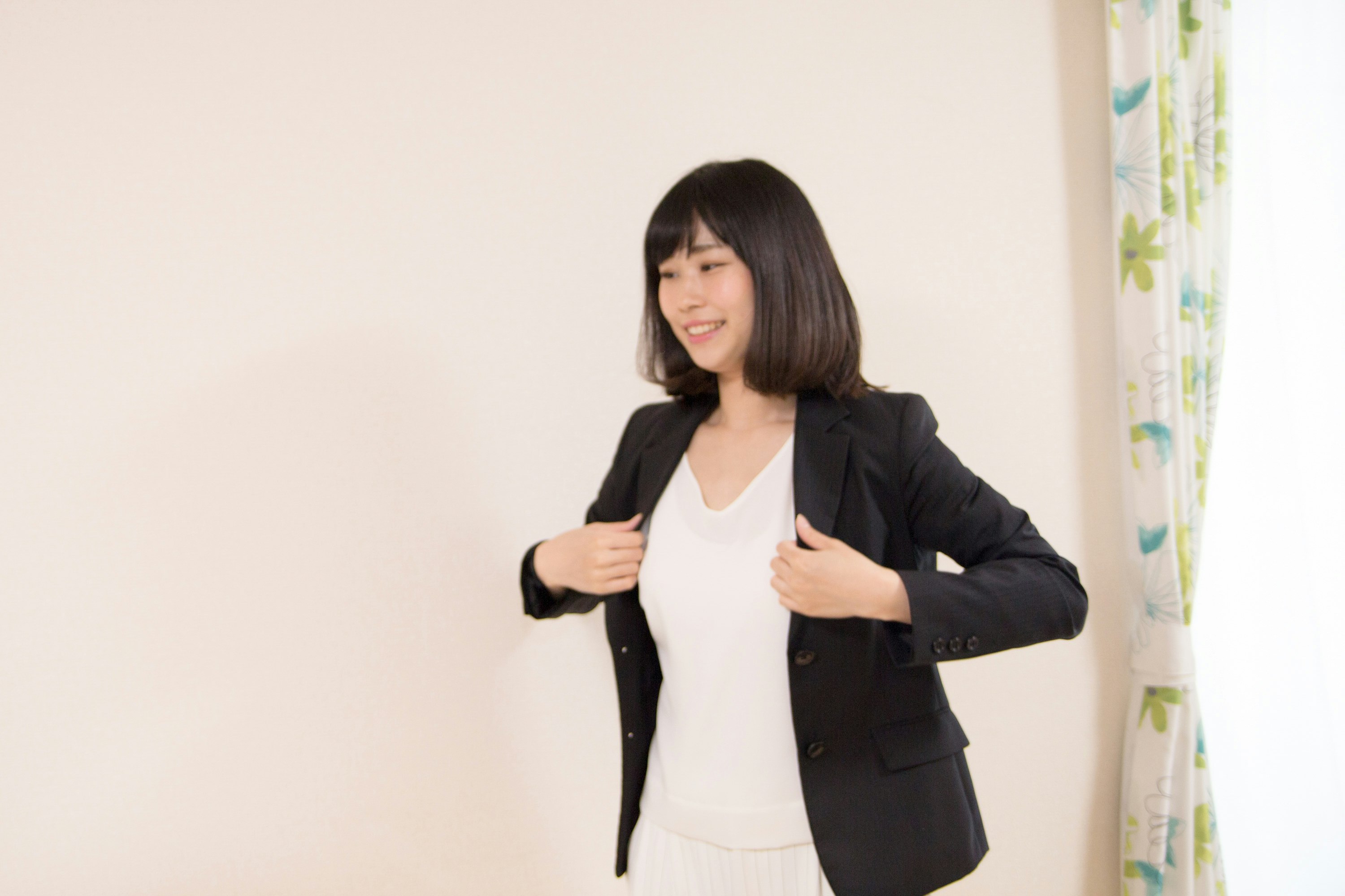 femme ajustant un blazer devant un mur clair