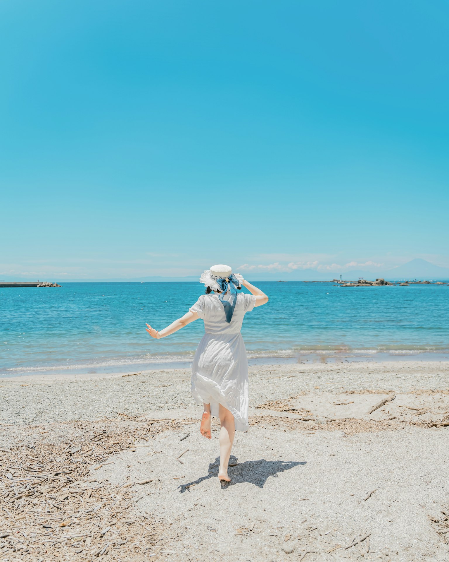 Una mujer con un vestido blanco corriendo hacia el mar bajo un cielo azul