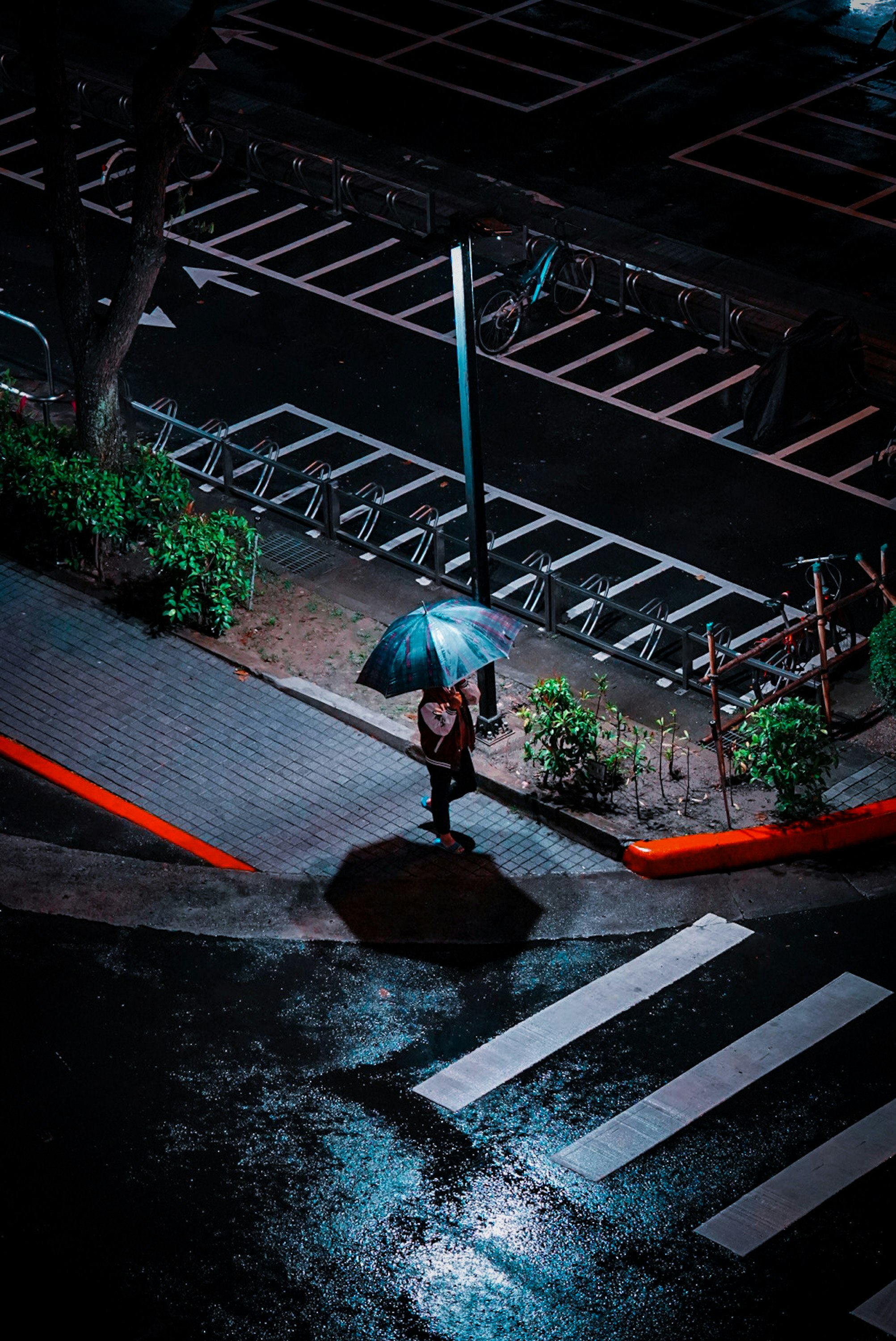 雨の夜、傘をさした人と街灯のある交差点の歩道
