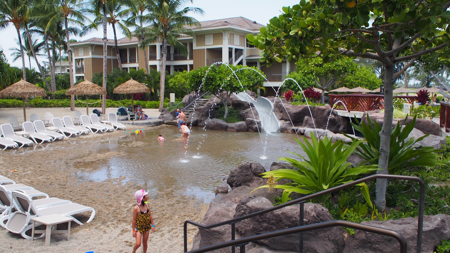Bambini che giocano in un'area piscina di un resort con una cascata e vegetazione lussureggiante