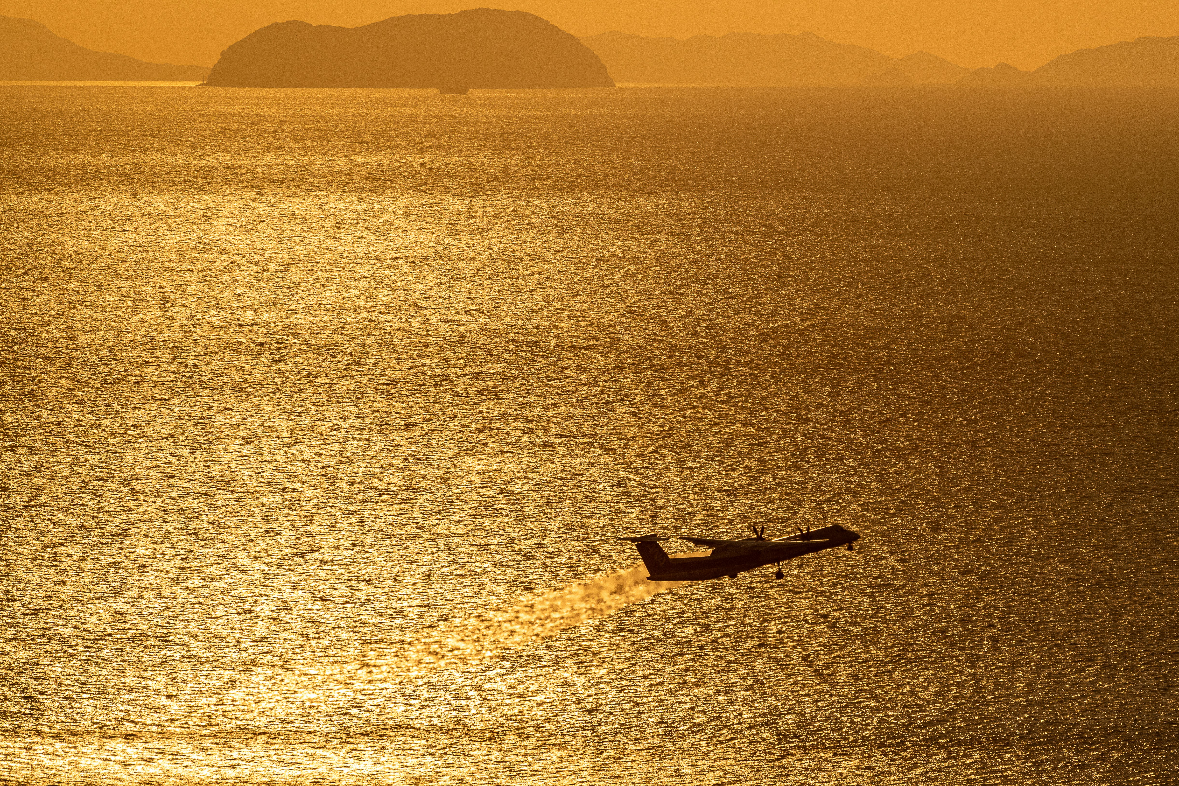 夕日に照らされた瀬戸内海と松山空港を望む山上からの飛行機の離陸