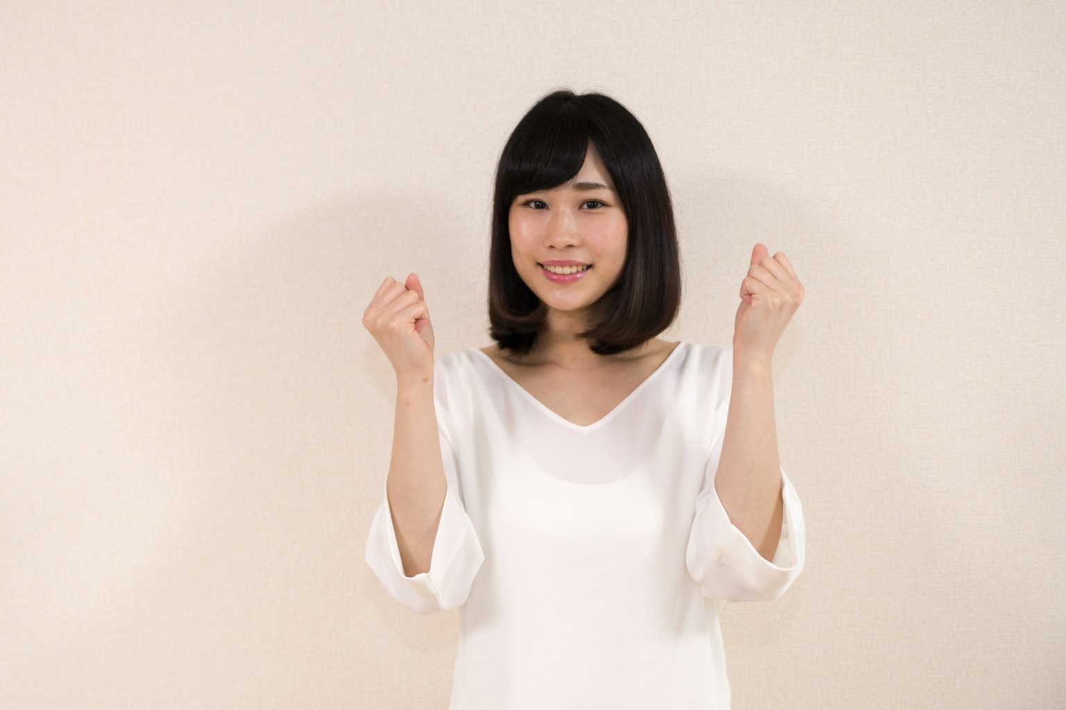 A woman in a white top smiling with her hands raised