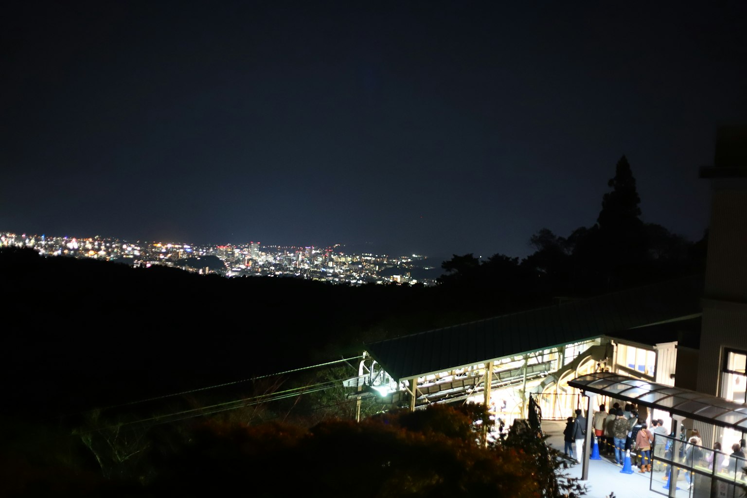 ภายนอกสถานีที่มีแสงไฟของเมืองในตอนกลางคืนและภูเขารอบข้าง