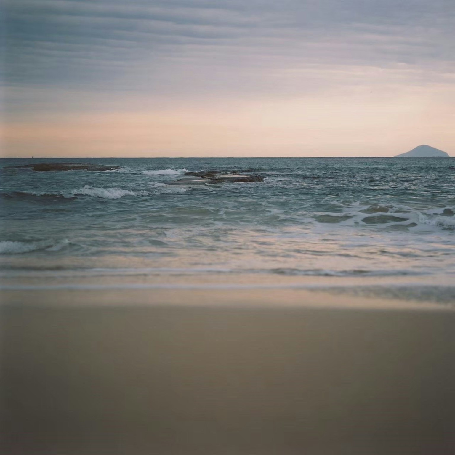 ทิวทัศน์ชายหาดทรายและมหาสมุทรที่สงบ ท้องฟ้ามีเมฆและภูเขาในระยะไกล