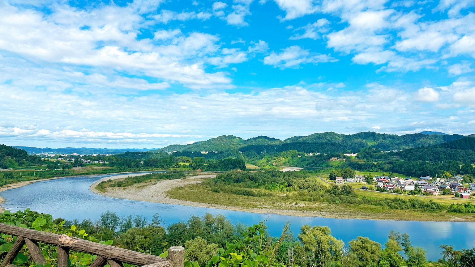 Scenic view of a river flowing through lush green hills under a bright blue sky