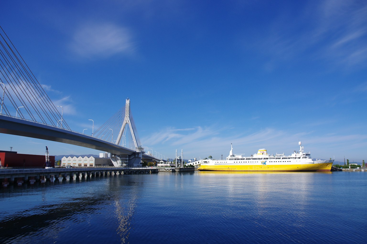 Harbor scene featuring a yellow ship and a modern bridge under a blue sky