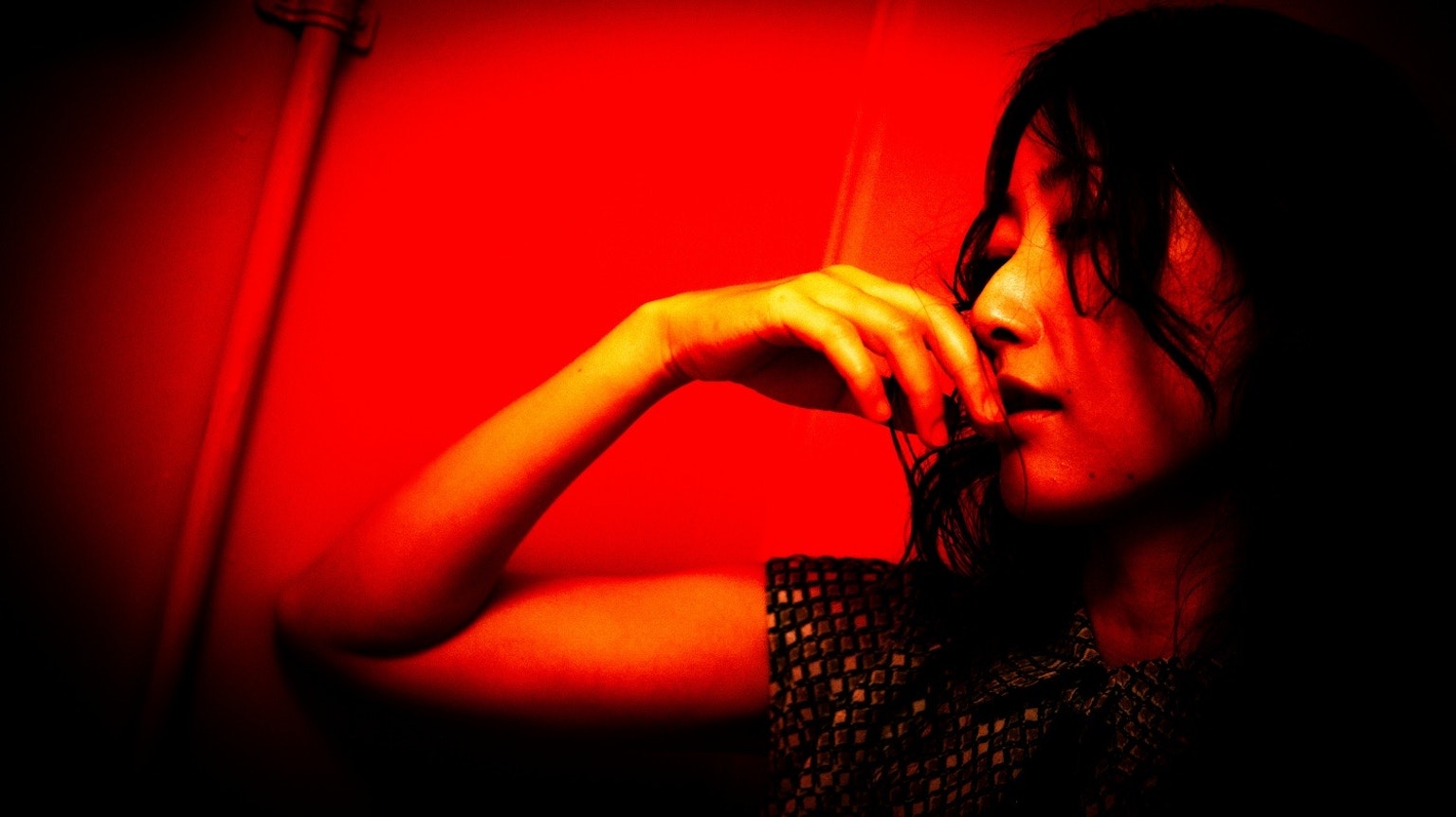 赤い背景の中で指を口に当てる女性の横顔