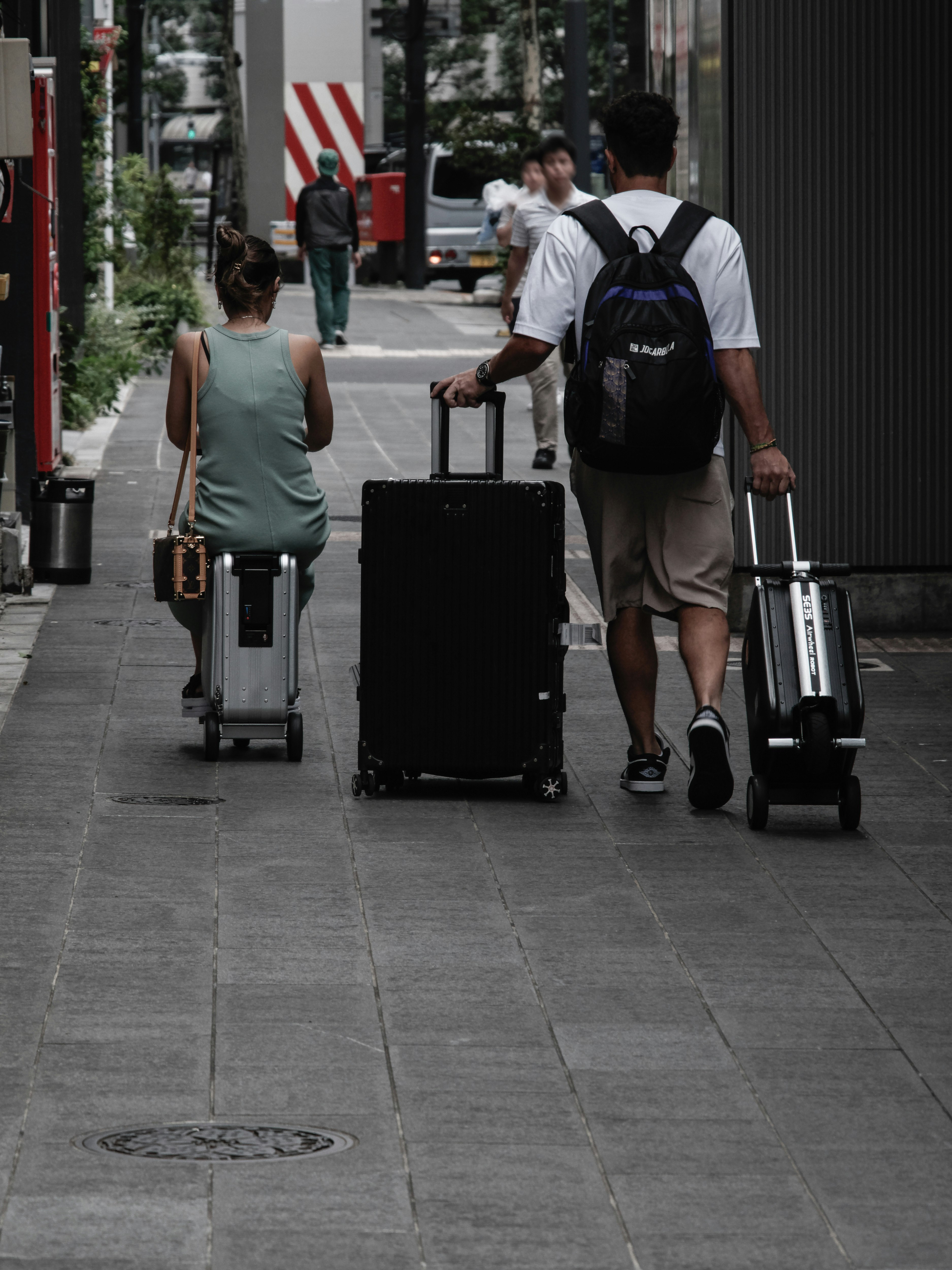電動スーツケースを引く旅行者のいる街の歩道