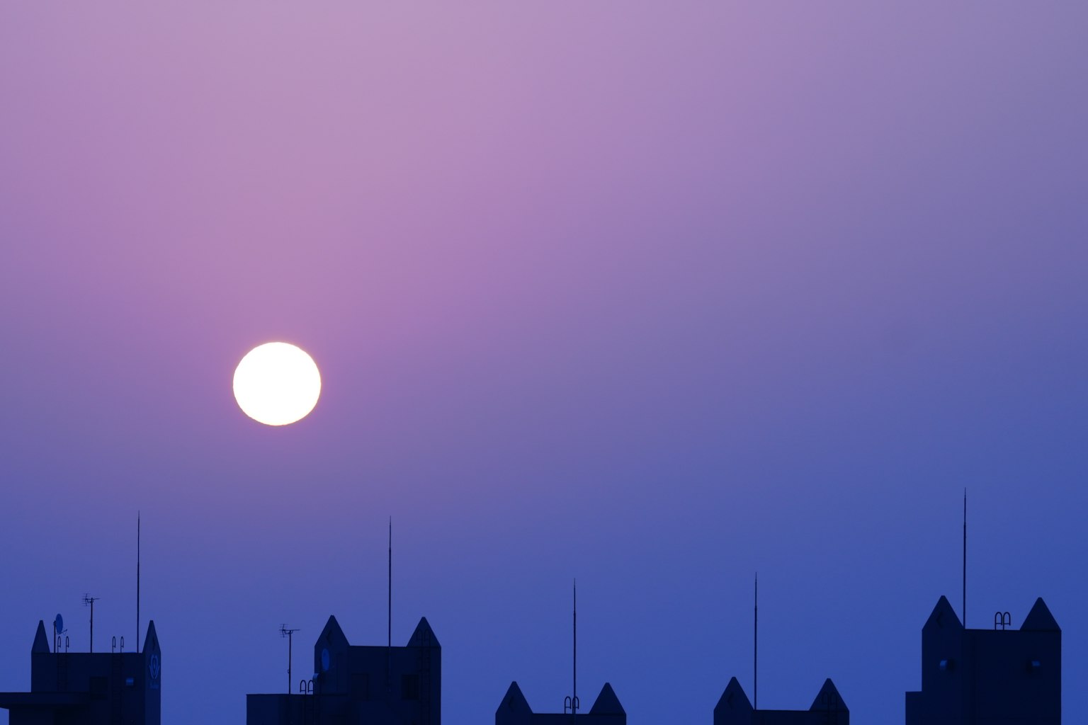 Sole grande che tramonta in un cielo viola con silhouette di edifici