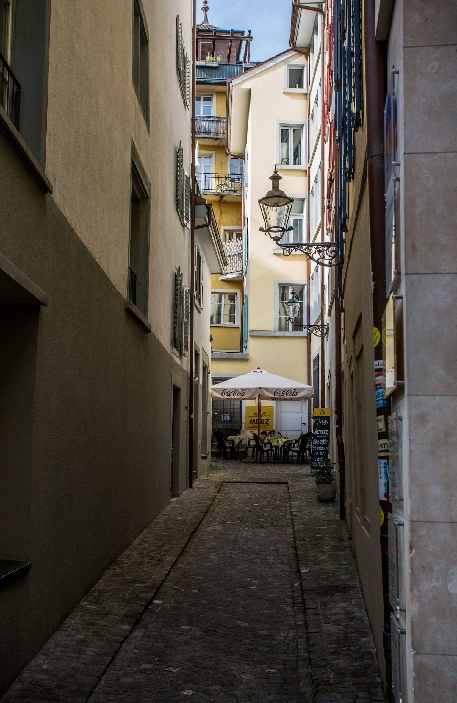 Vicolo stretto con un tavolo da caffè sotto un ombrello e edifici circostanti