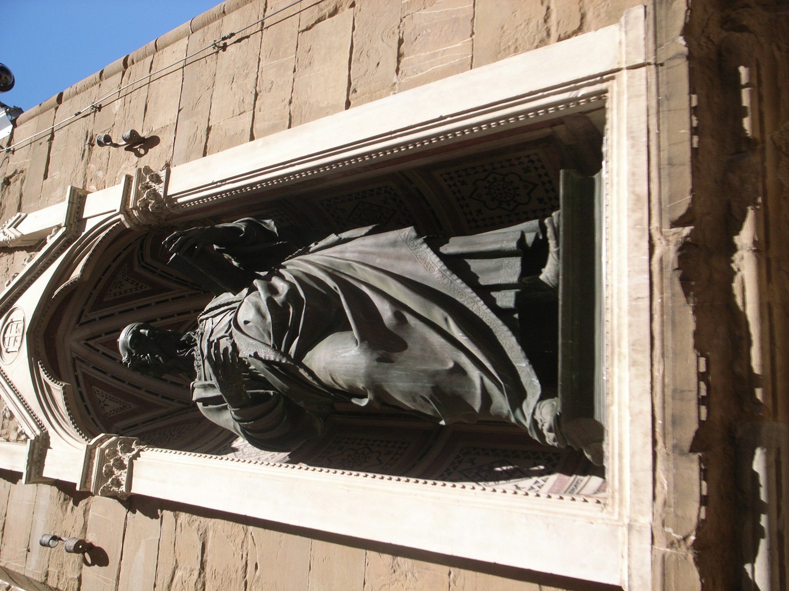 Una figura scolpita di un santo su una facciata di edificio illuminata dalla luce del sole