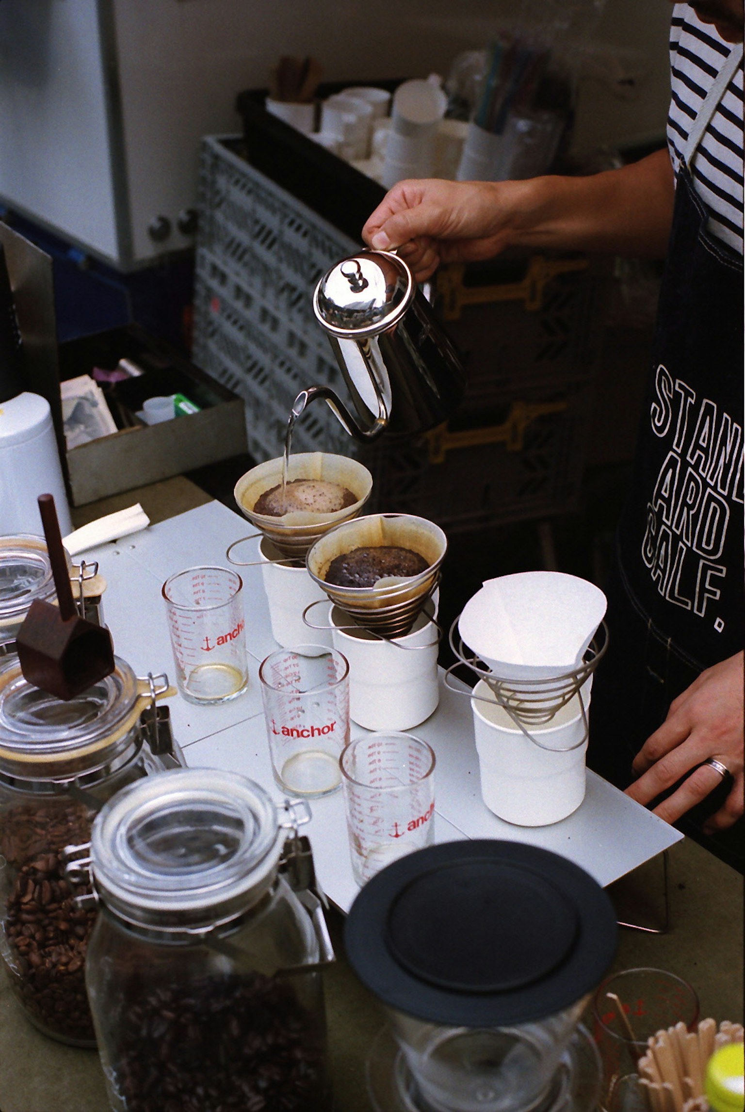 A barista pouring coffee into brewing devices with glass jars and coffee grounds