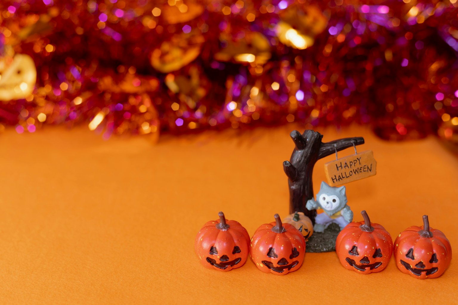 Decorazioni di Halloween con quattro zucche e una figurina di gatto su uno sfondo arancione