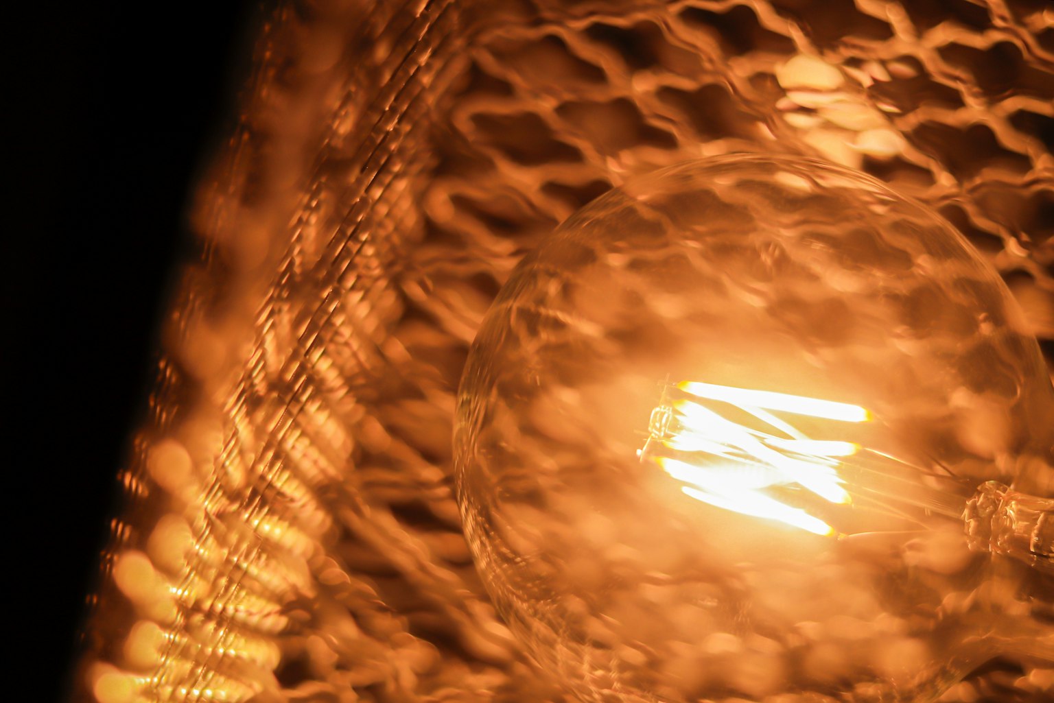 A warm orange light bulb inside a mesh shade