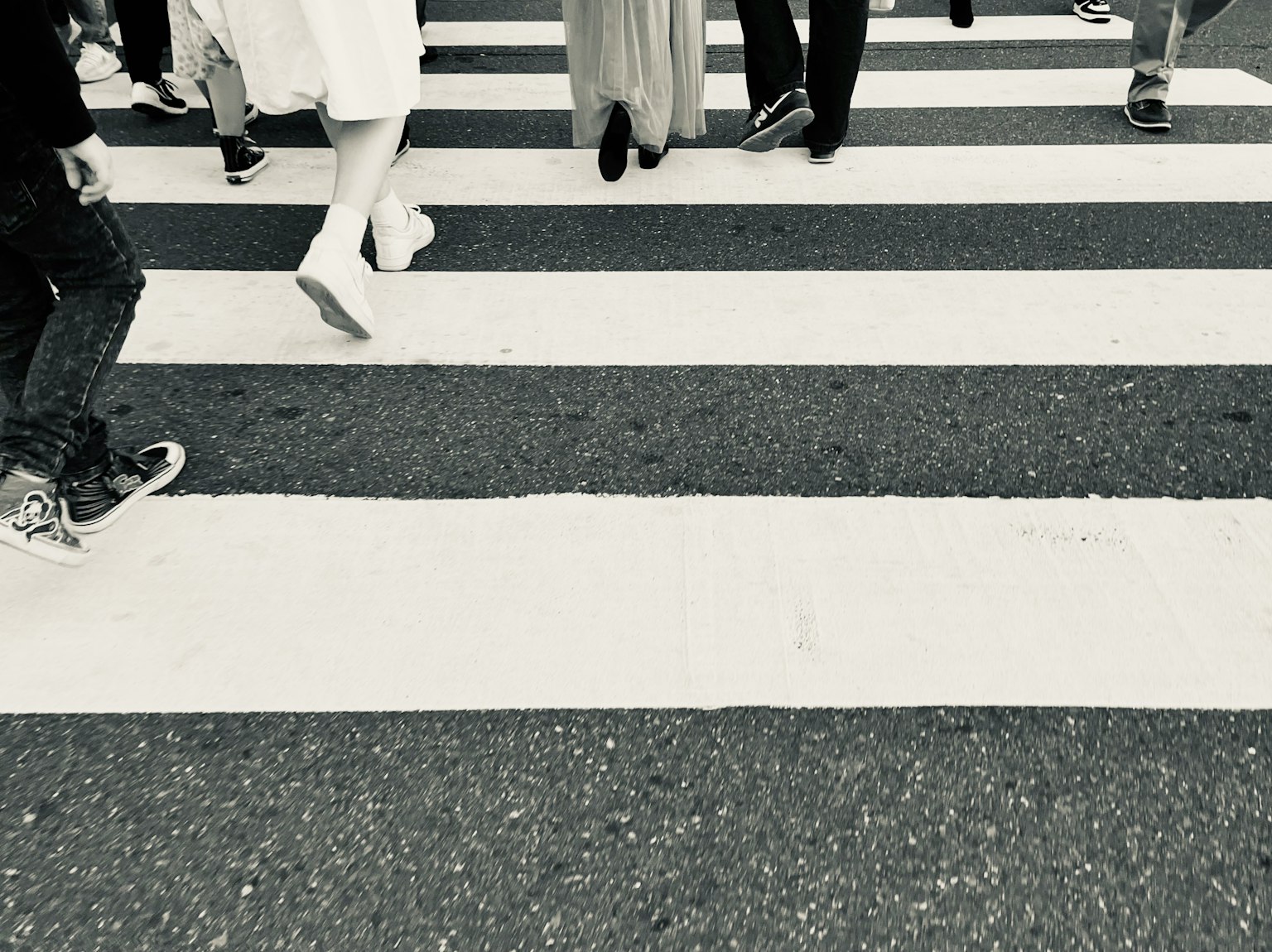 Feet of pedestrians crossing a black and white crosswalk