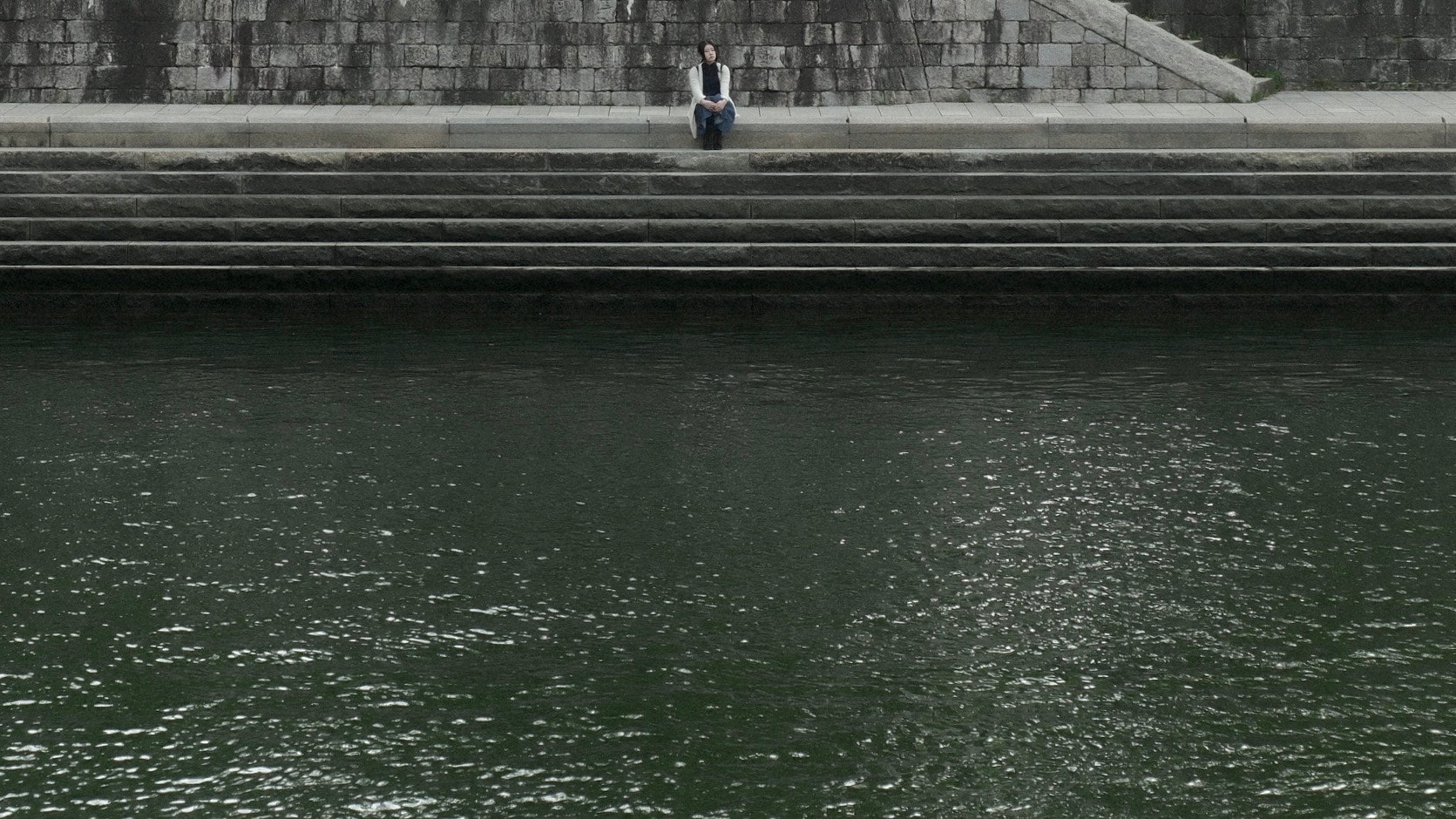 A person sitting by the quiet water with steps in the background