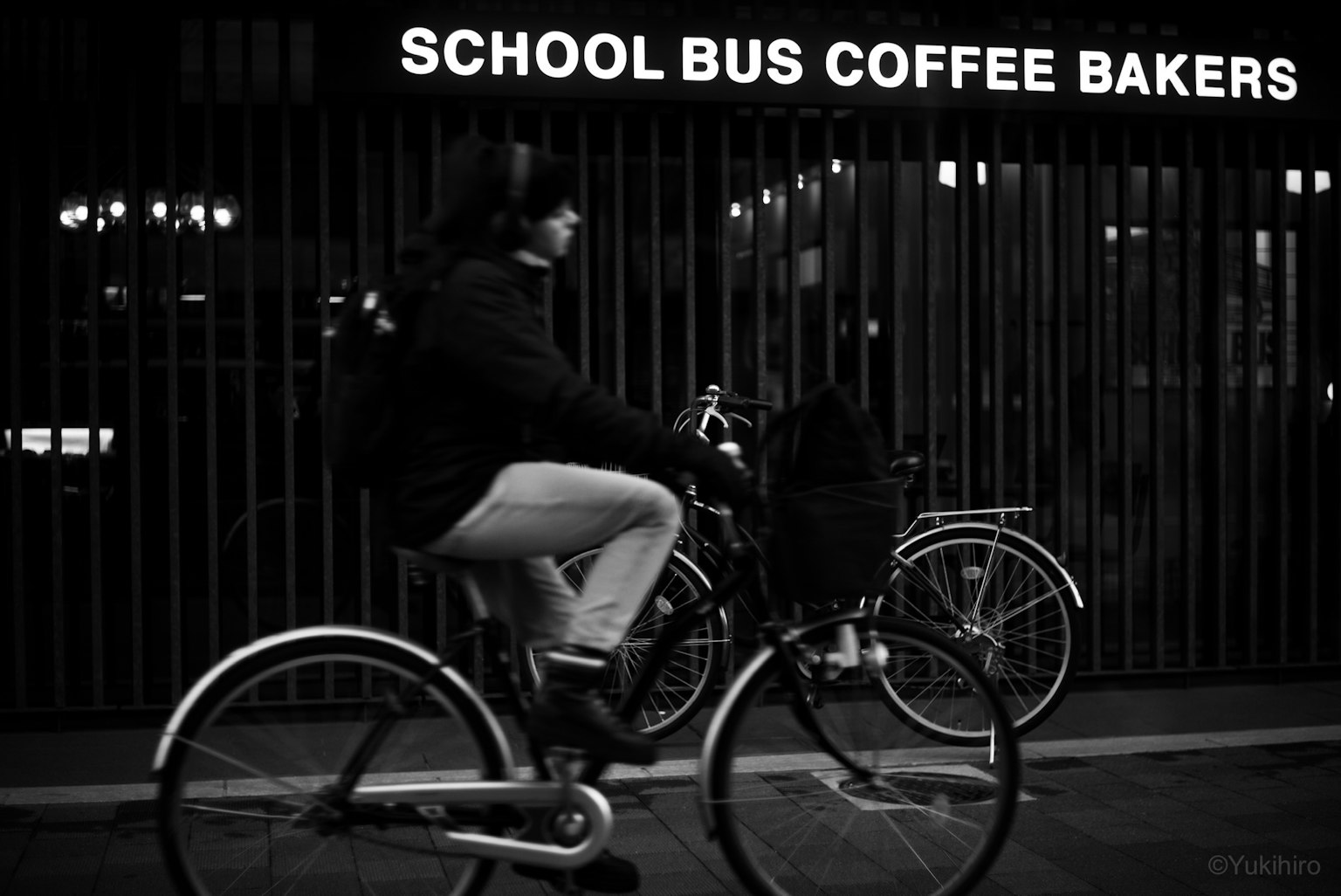 Una scena di strada in bianco e nero con un ciclista e un'insegna di caffè sullo sfondo