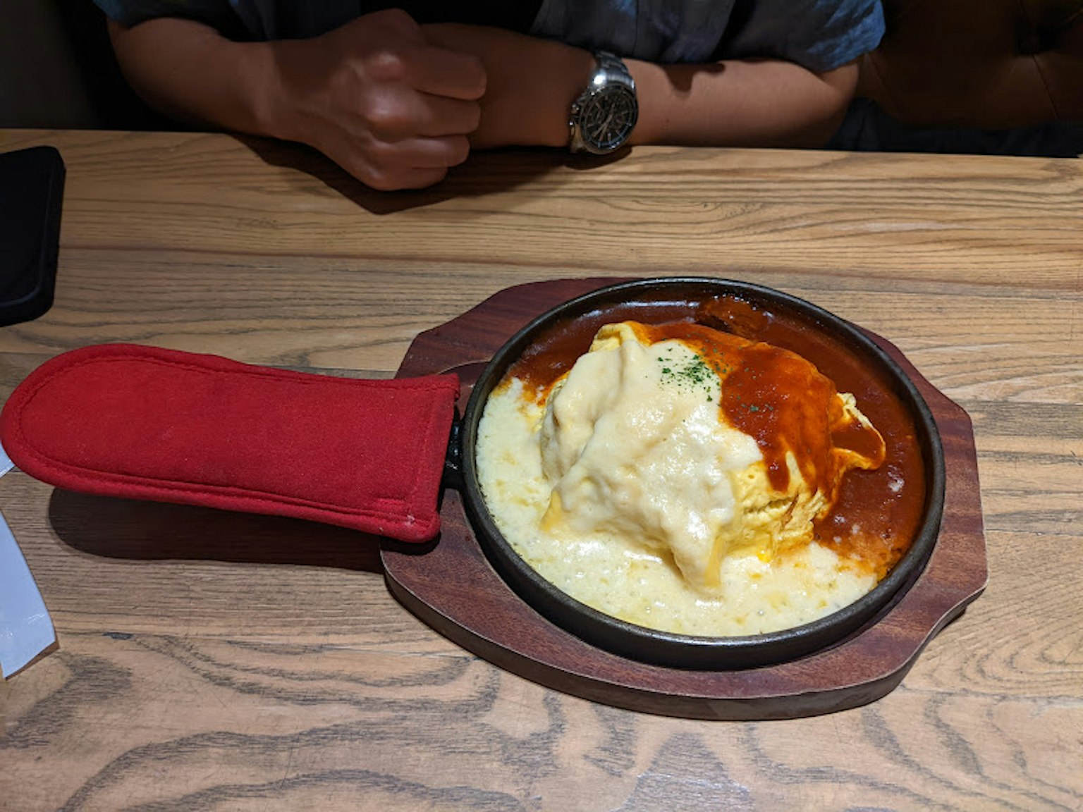 Omelette rice topped with cheese in a skillet with a red mitt