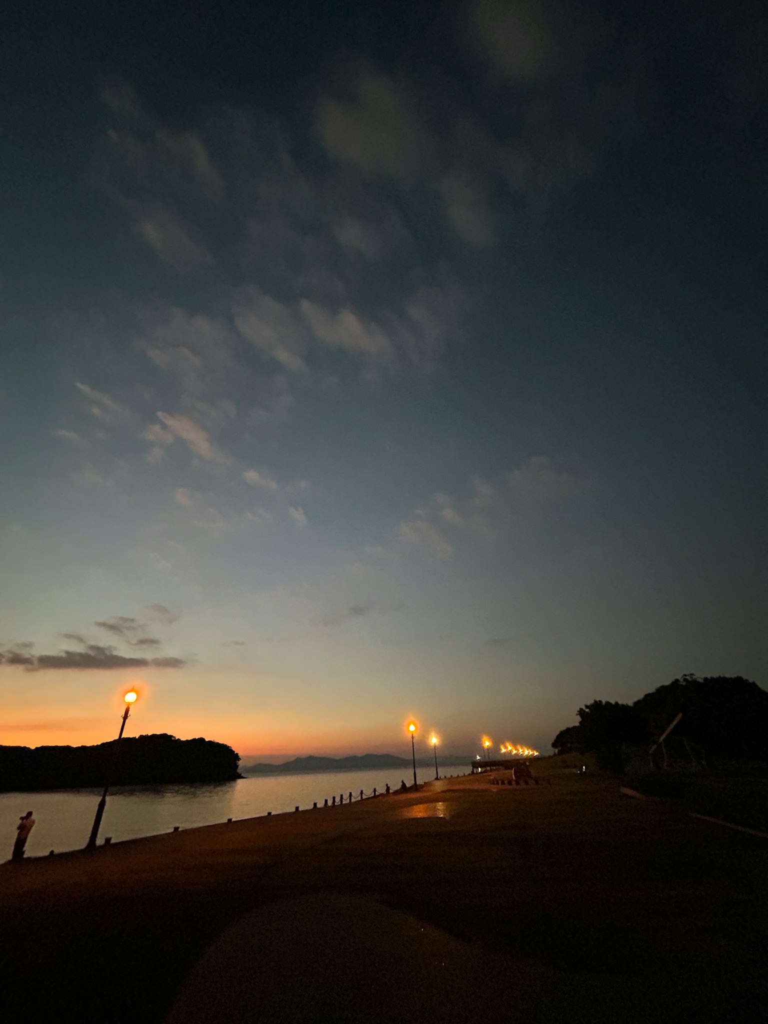 Pemandangan malam yang tenang di pantai dengan matahari terbenam dan lampu jalan yang bersinar