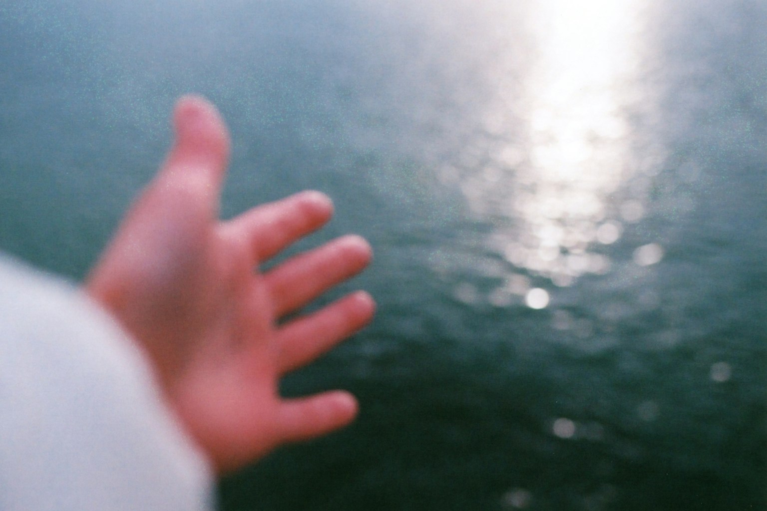 Immagine sfocata di una mano che si allunga verso la superficie dell'acqua