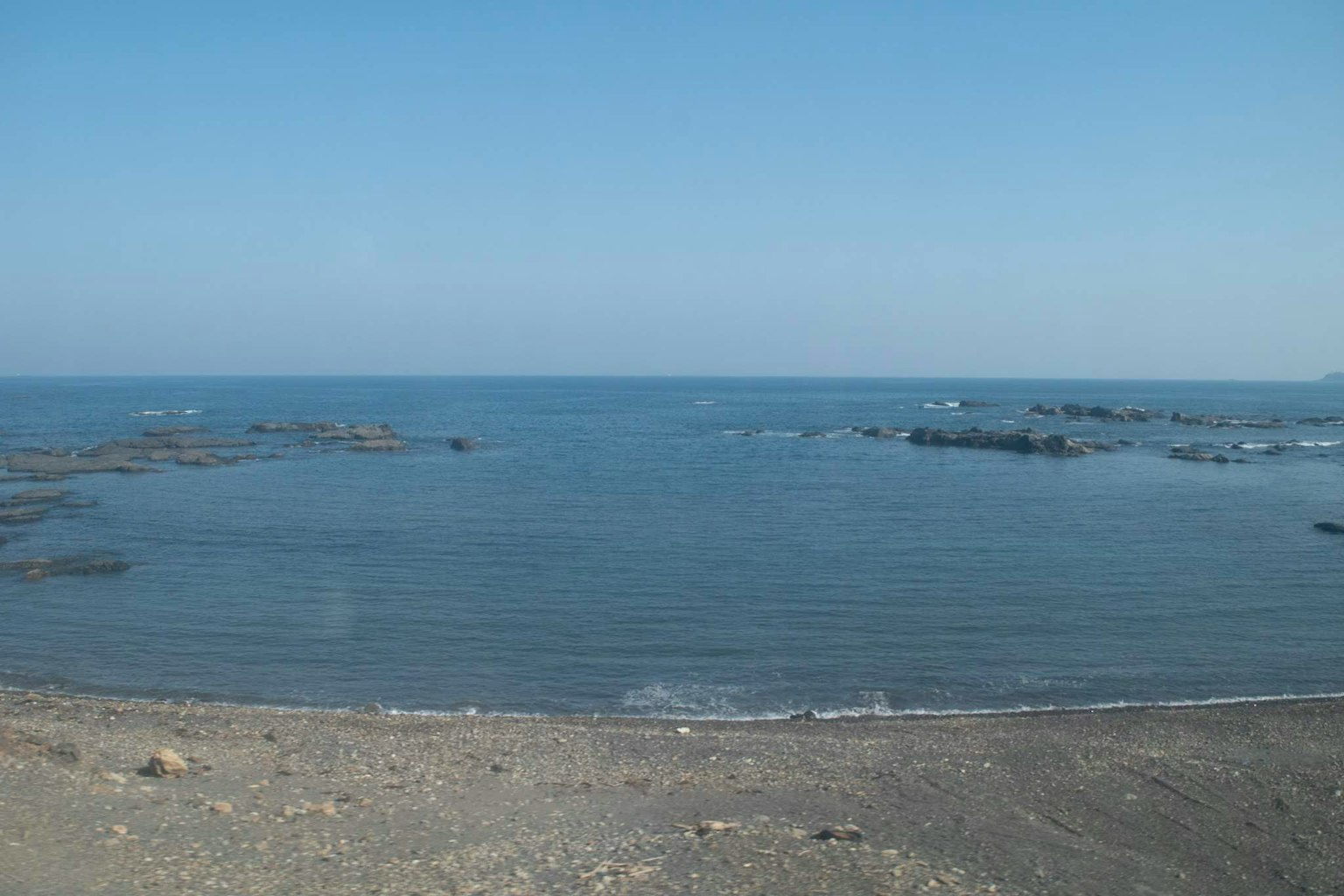 Vista de un mar tranquilo y un cielo azul con una costa rocosa visible