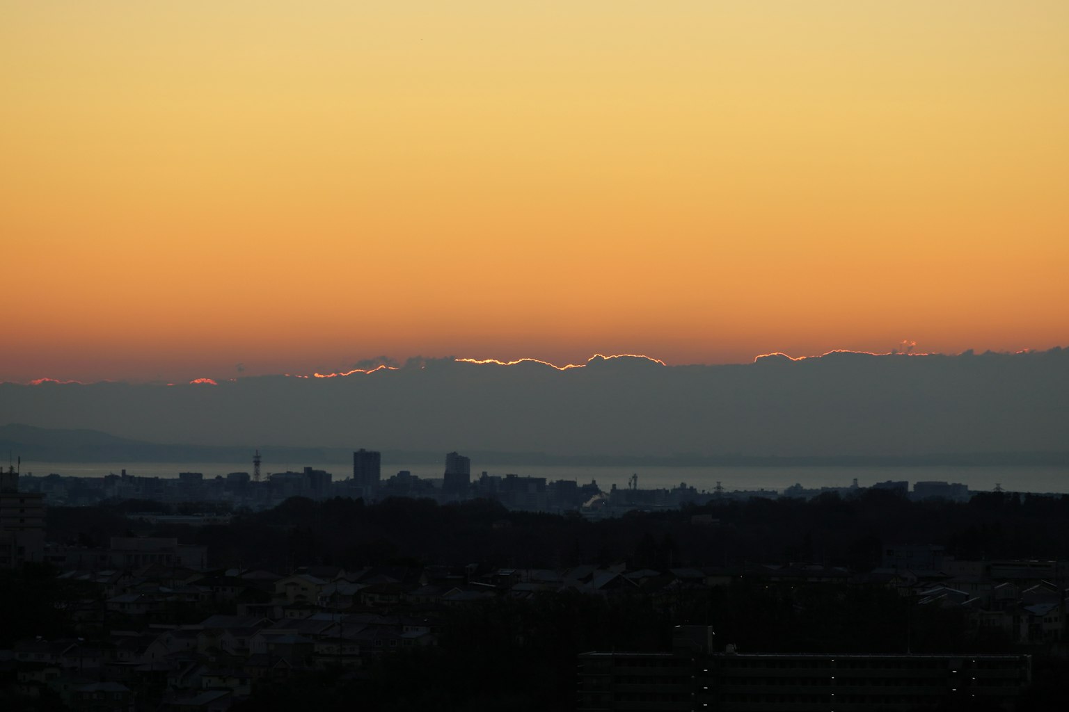 City skyline silhouetted against a sunset with mountains in the background