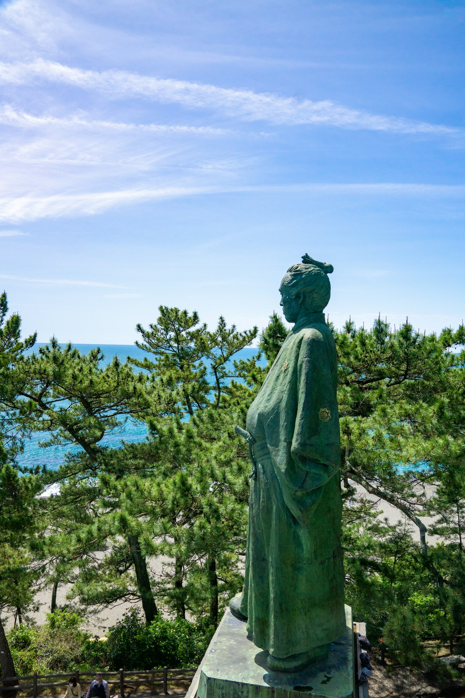 Estatua verde que mira al mar con árboles de fondo