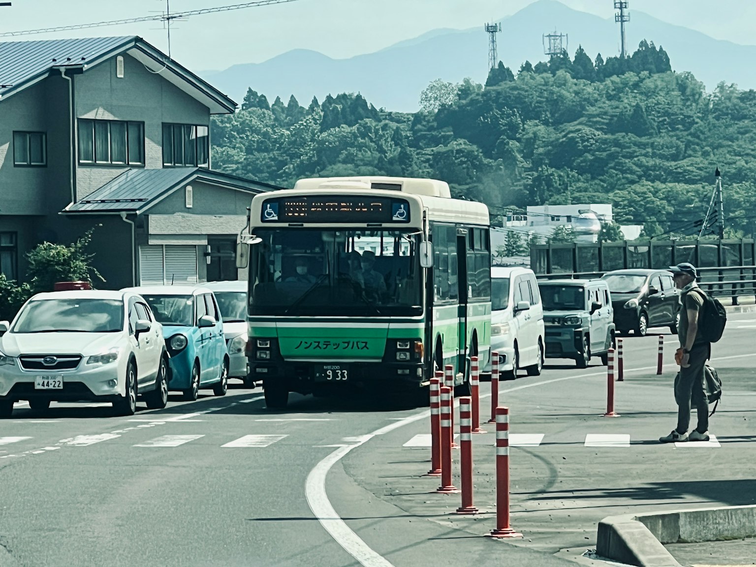 一輛公車在站牌等候，周圍是汽車和背景中的山脈