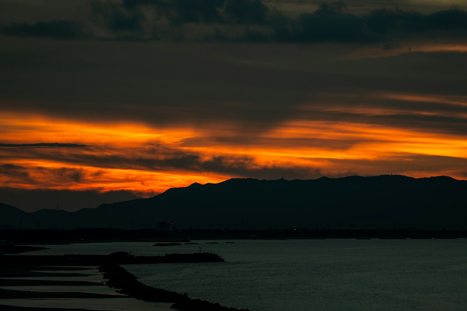 Scenic view of a sunset with orange hues in the sky and silhouette of mountains over water