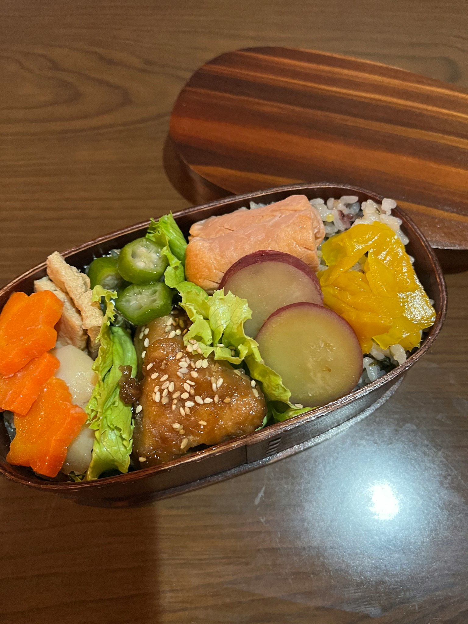 一个便当盒，里面装满了各种食材，包括三文鱼、蔬菜和米饭