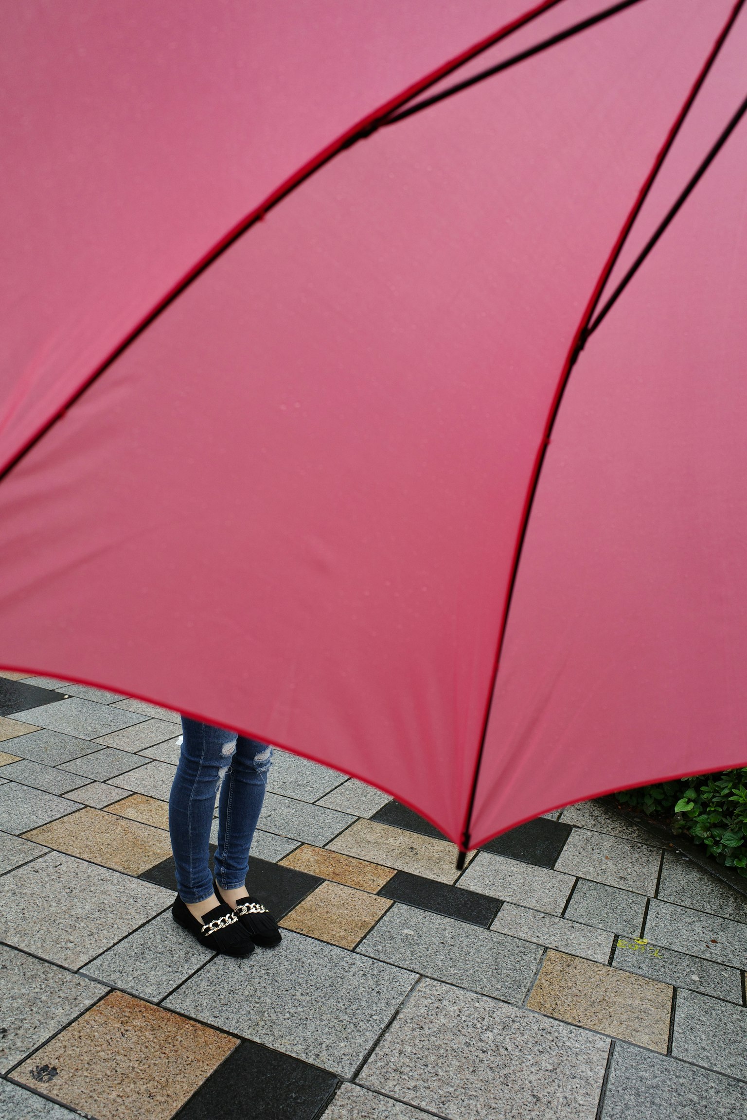 Una persona de pie bajo un paraguas rojo con pies visibles