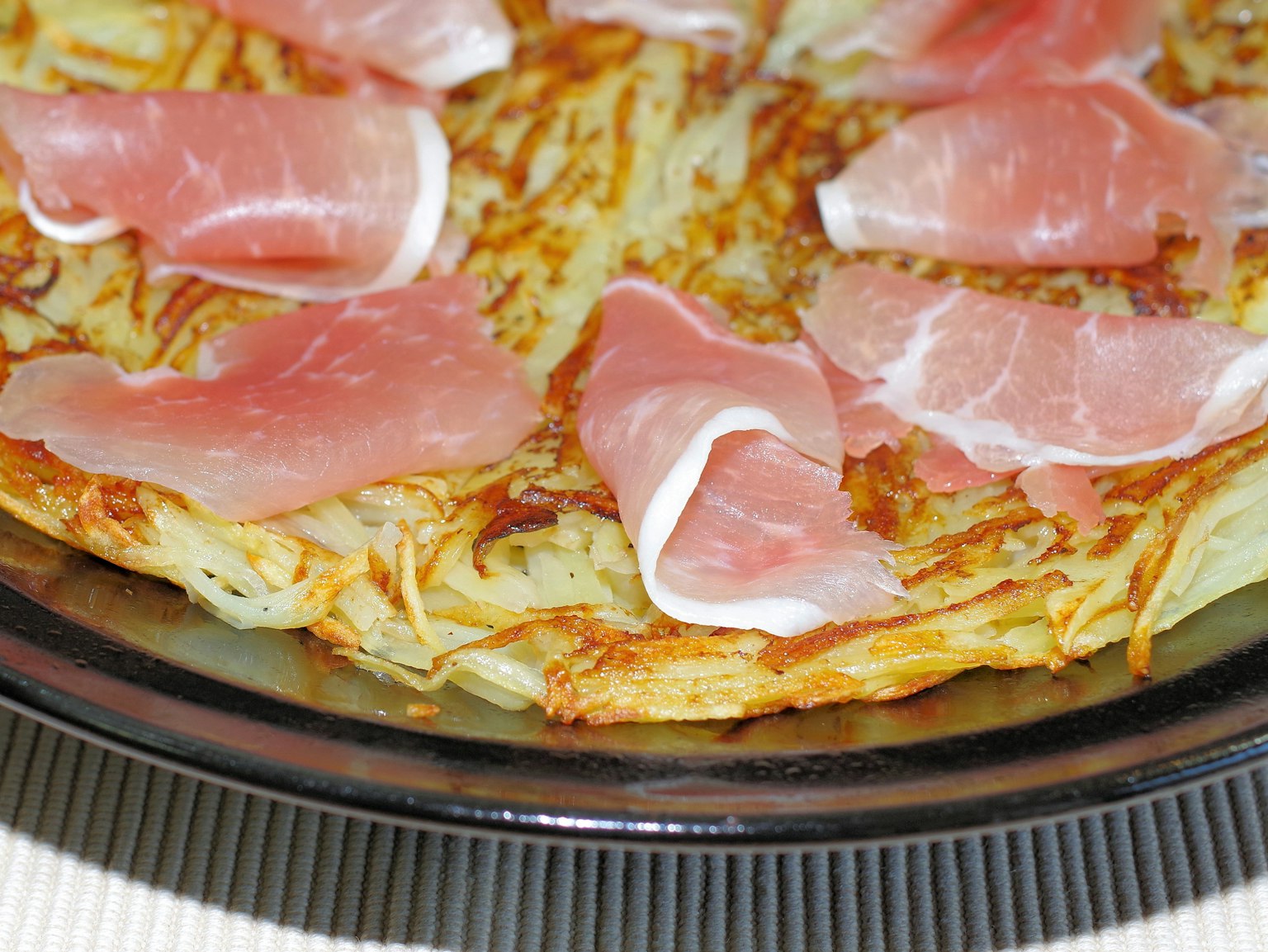 Piatto di patate croccanti guarnito con fette di prosciutto