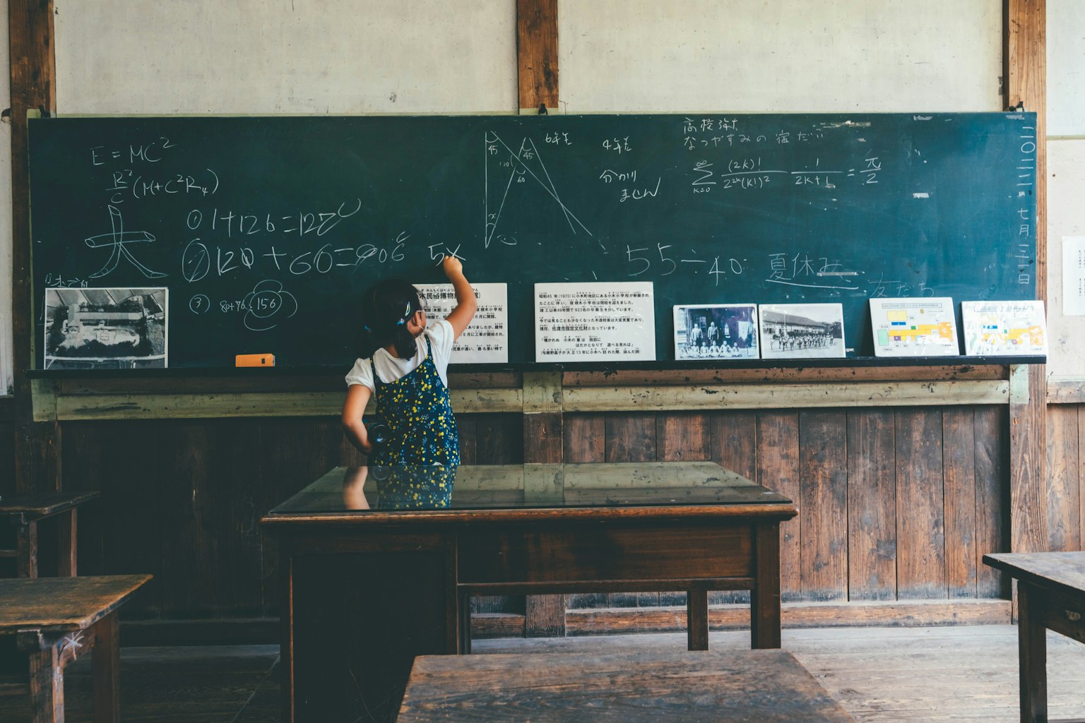 Une femme debout devant un tableau noir dans une salle de classe avec des bureaux en bois