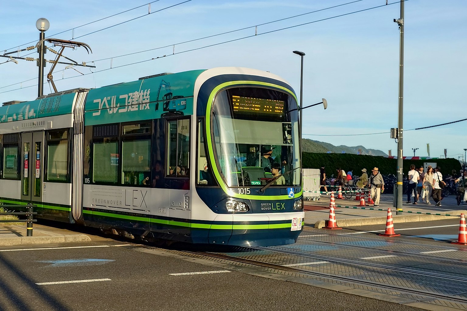 Blau-grüner Straßenbahn an einer Haltestelle mit Menschen