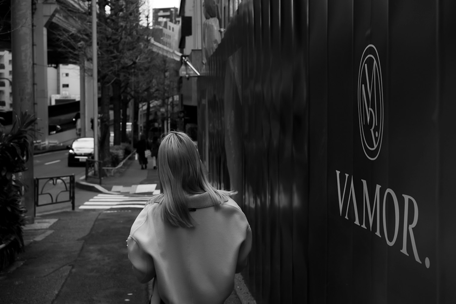 Una mujer caminando de espaldas en un entorno urbano Fondo en blanco y negro con el logo VAMOR