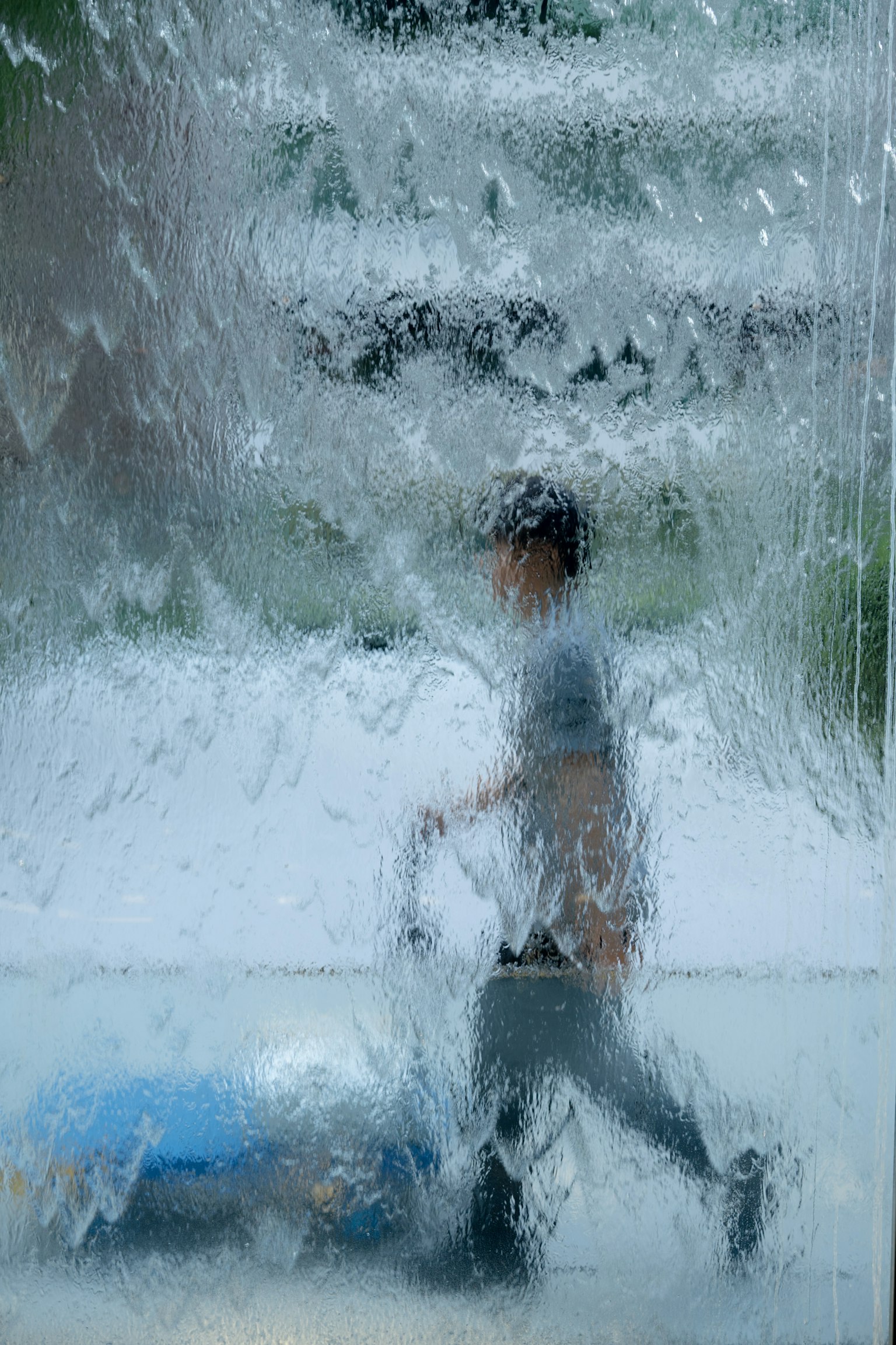 水のような質感のガラス越しに歩く人のシルエット