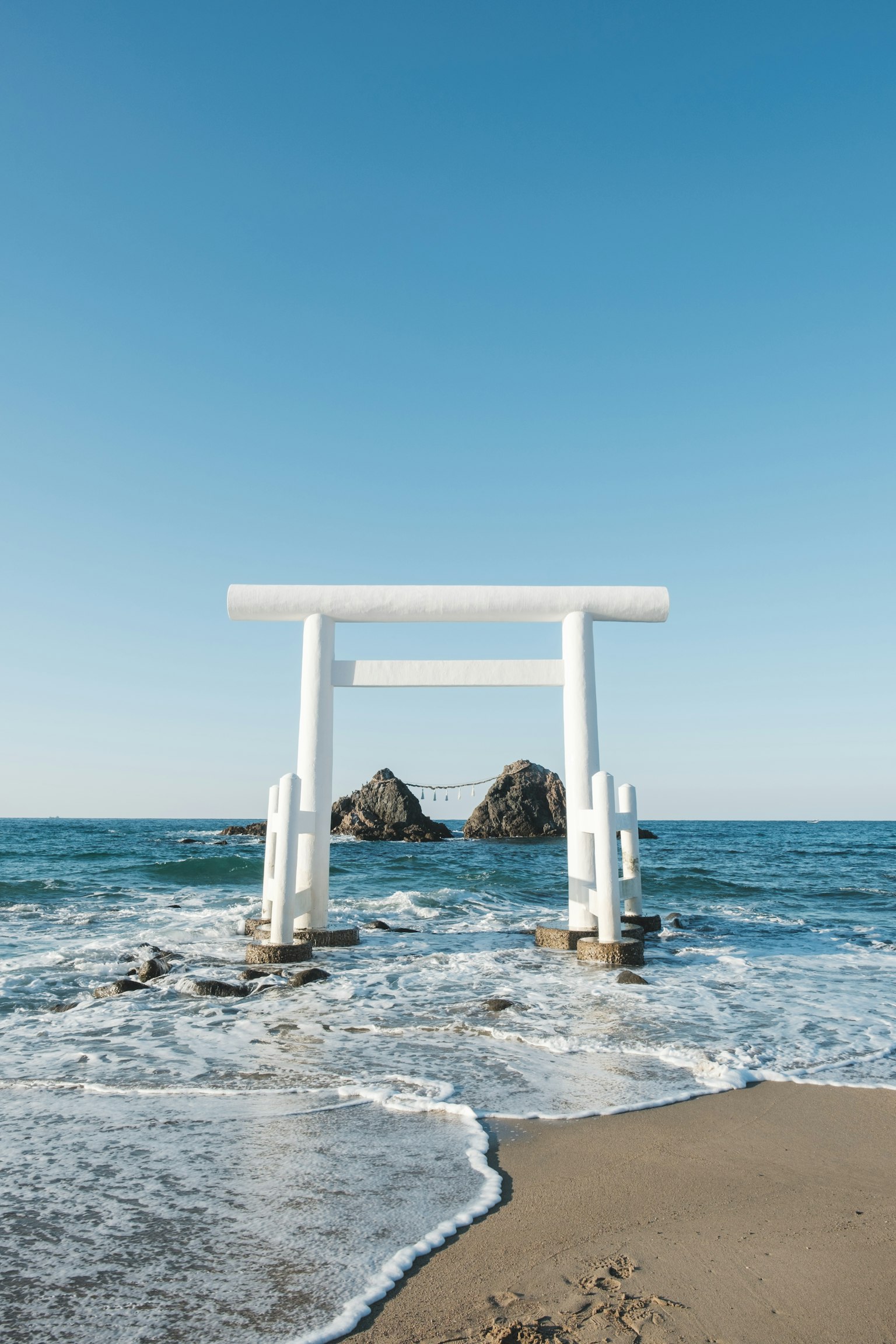 Gerbang torii putih di tepi laut dengan ombak dan batu