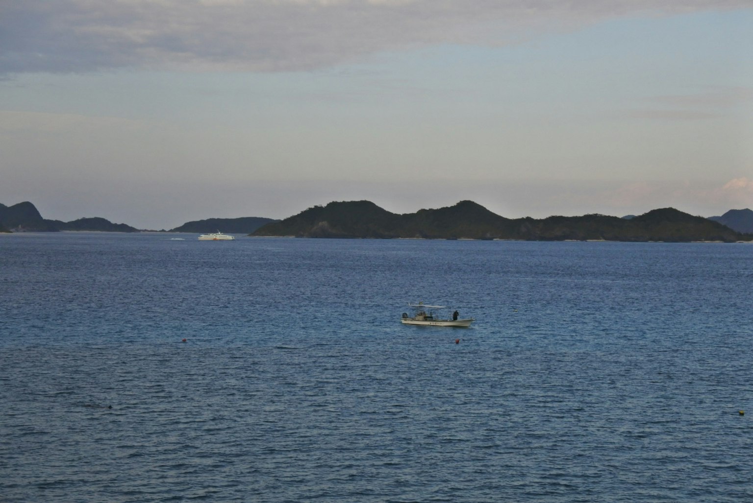 Vista panoramica dell'oceano blu con una piccola barca e isole lontane