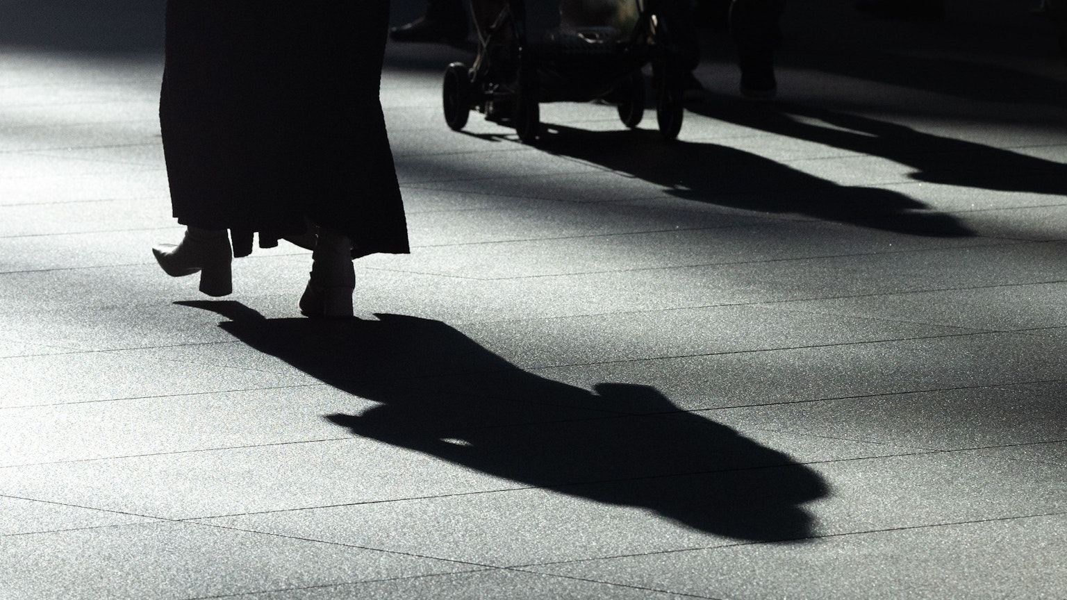 Une personne en vêtements noirs marchant avec une ombre projetée sur le trottoir