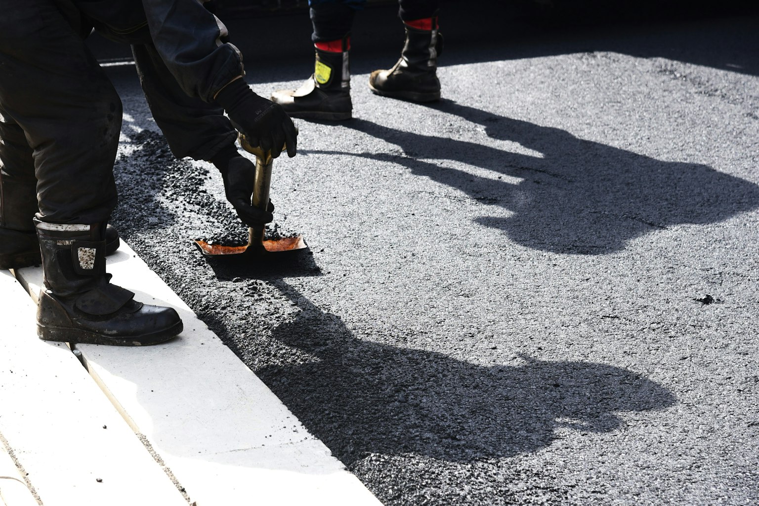 Workers applying asphalt with tools and shadows on the surface