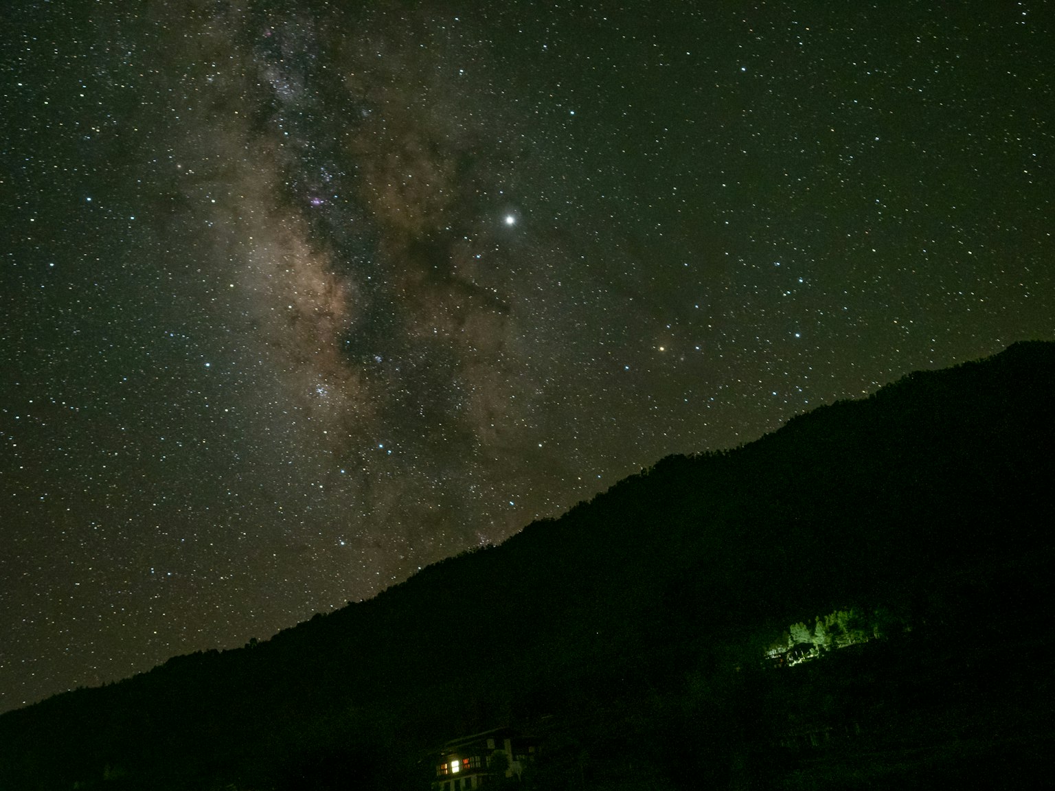 夜空的壮丽景观，银河山的轮廓被远处的灯光照亮