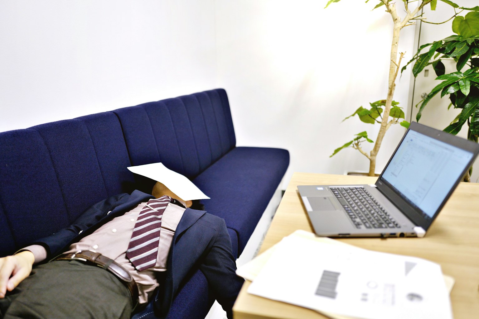 Doanh nhân nằm trên ghế sofa màu xanh lam với laptop gần đó