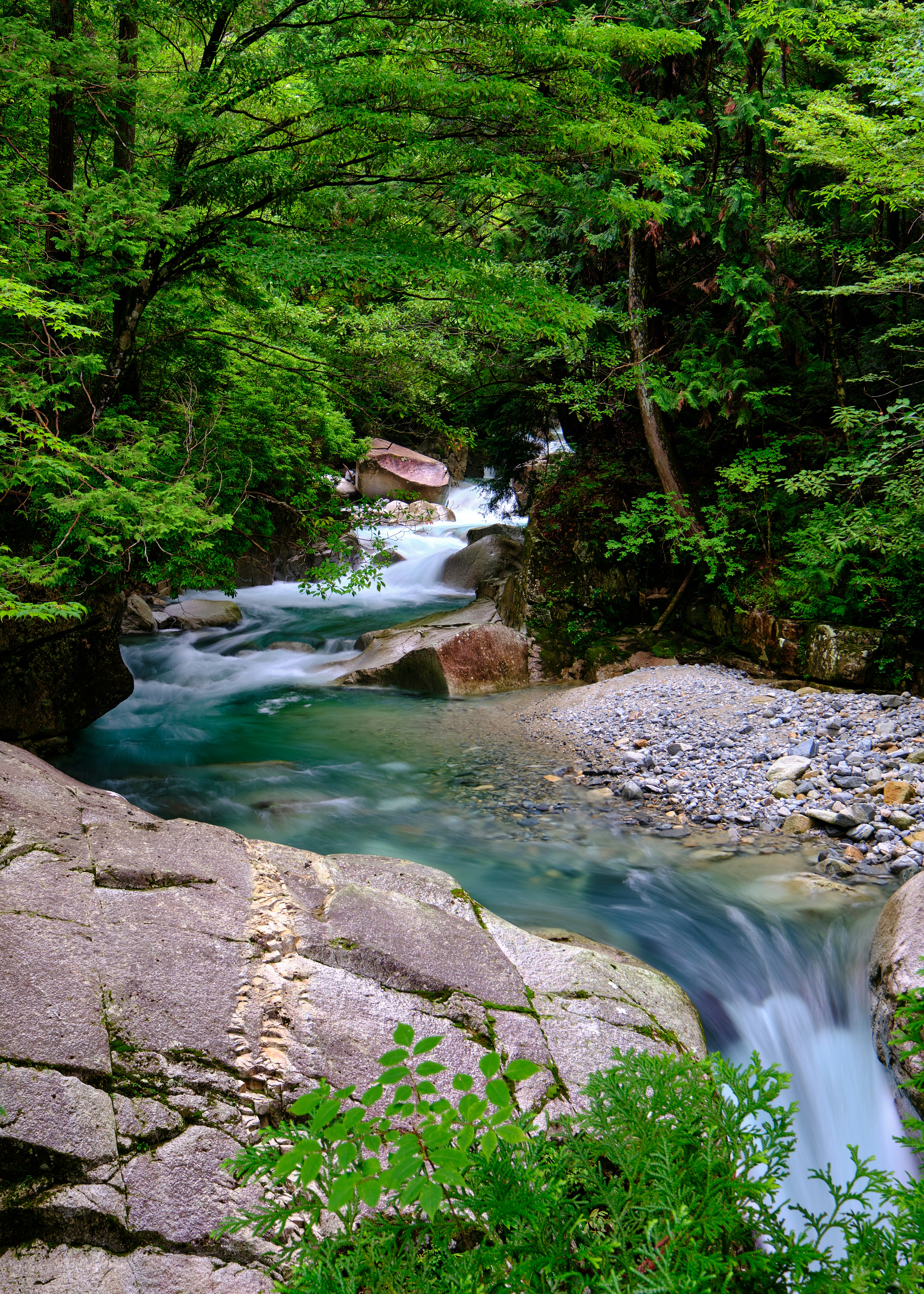 klarer Fluss und kleine Wasserfälle in einem grünen Tal
