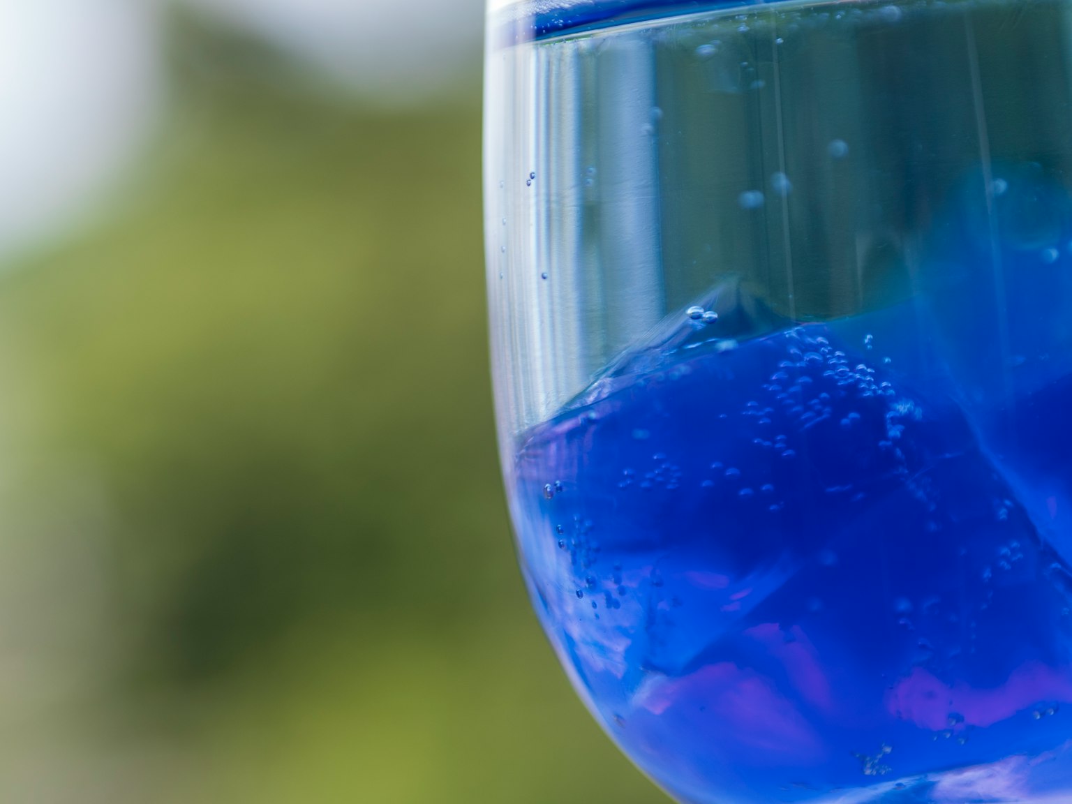 Gros plan d'une boisson bleue dans un verre transparent avec un arrière-plan vert flou