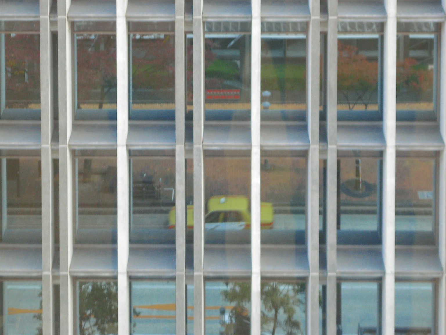 ガラスのビルの反射に映る黄色いタクシーと周囲の景色