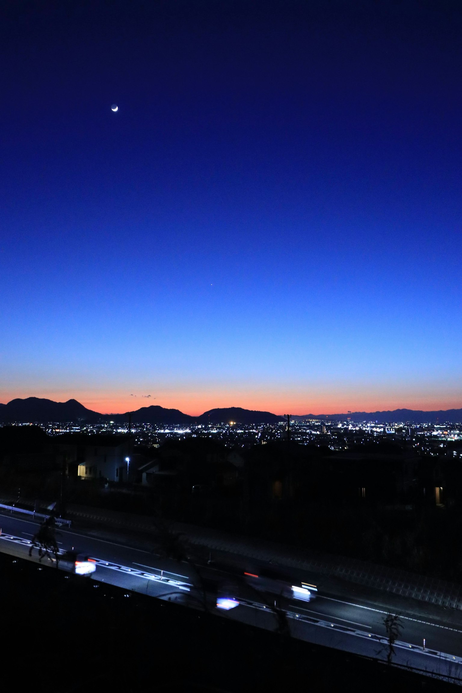 Twilight sky with a visible moon and city lights in the distance