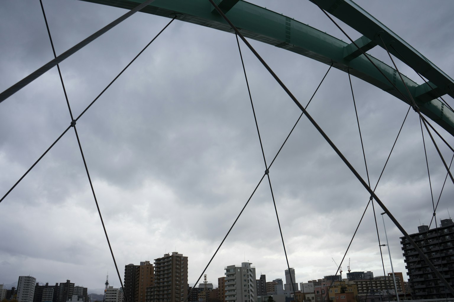 Estructura de puente en arco bajo un cielo nublado con horizonte urbano de fondo