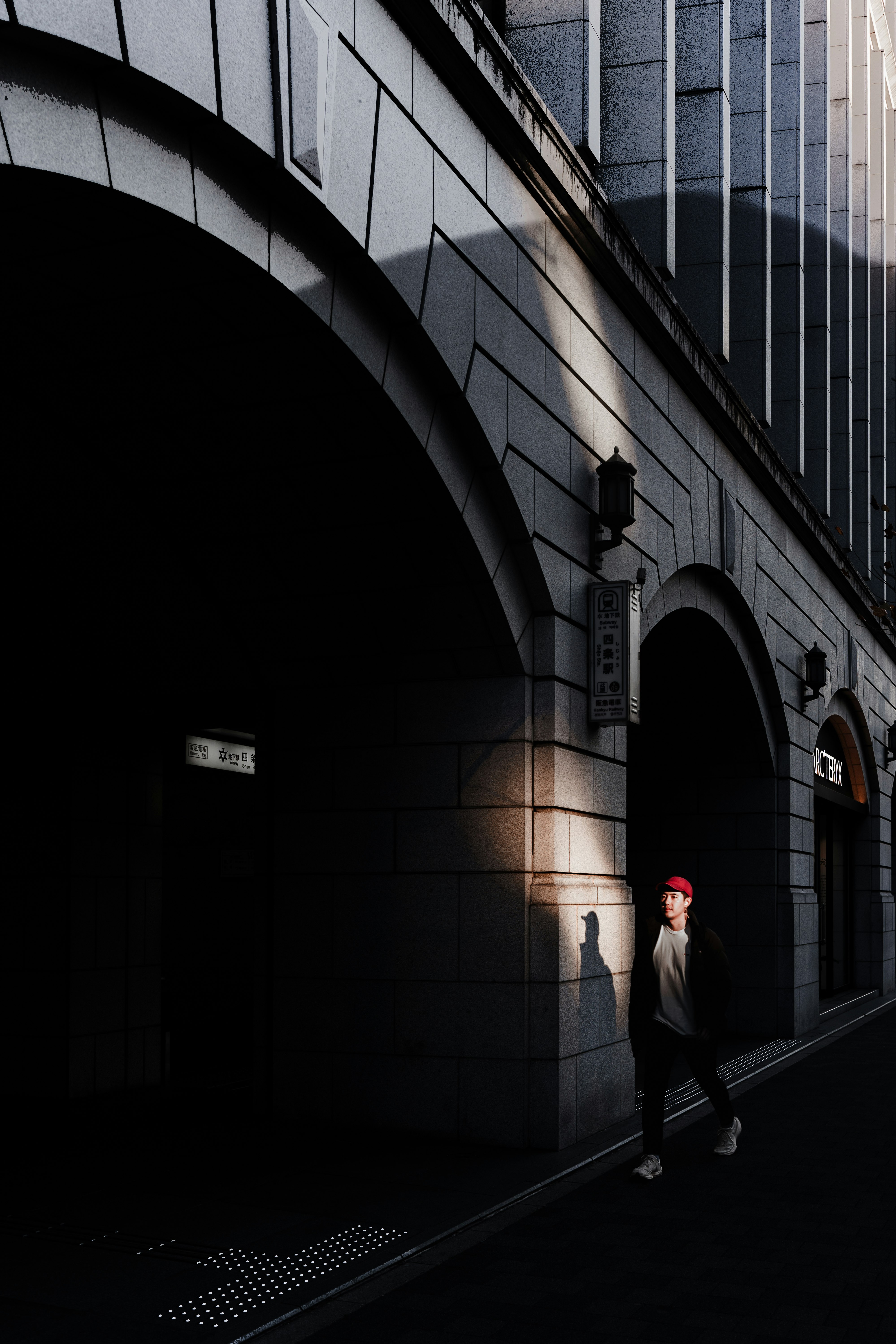 Arkaden-Gasse mit Straßenlaternen und Person mit rotem Hut